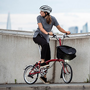 Imagebild des Brompton House Red, Frau mit Jeans und grauem Hemd sitzt auf dem Faltrad.