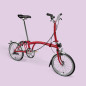 Preview: Das Brompton Faltrad House Red ist seitlich vor rosafarbigen Hintergrund abgebildet.