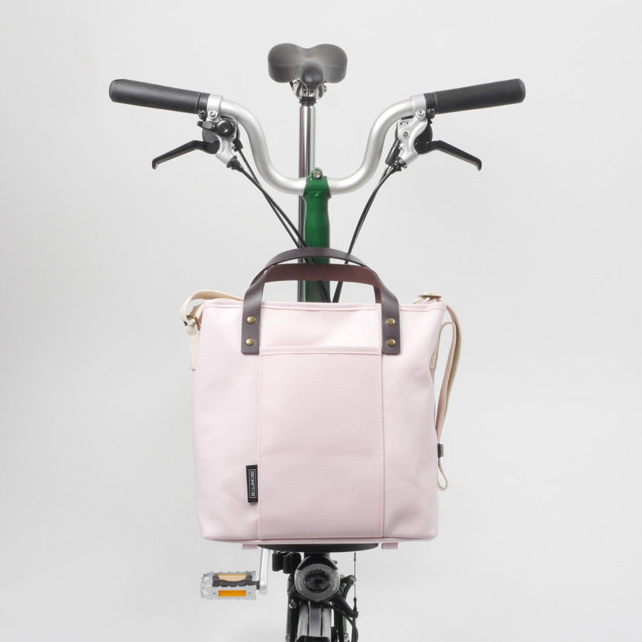 Die rosafarbige Tote Bag von Brompton ist auf den Front Carrier eines grünen Faltrades gesteckt und frontal von vorne abgelichtet