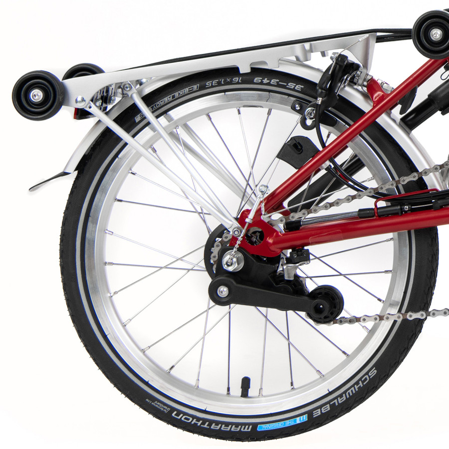 Das Hinterrad eines roten Brompton Faltrades ist mit Gepäckträger abgelichtet.