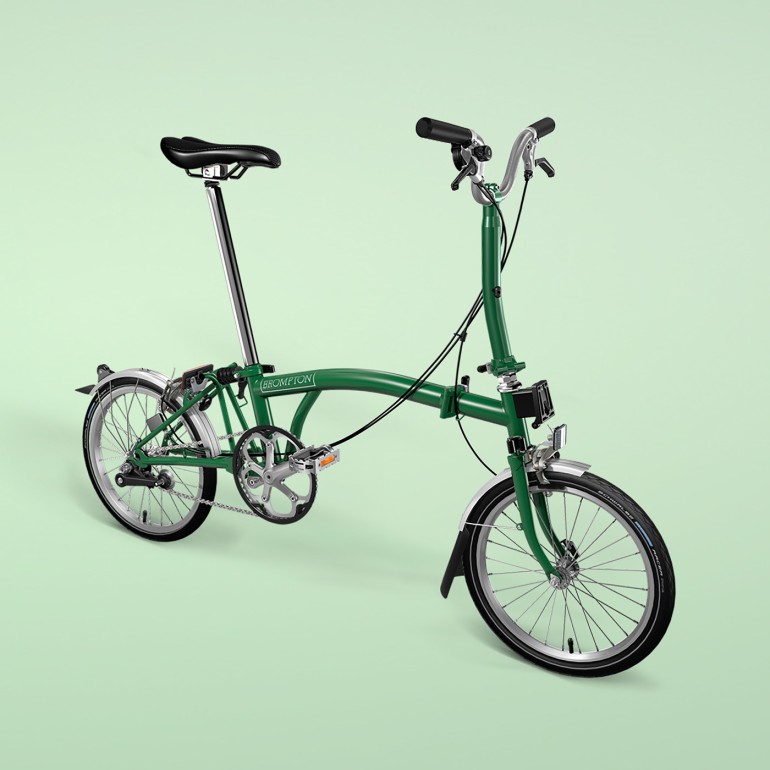 Ein grünes Brompton Faltrad M-Typ ist seitlich vor grünem Hintergrund aufgenommen.